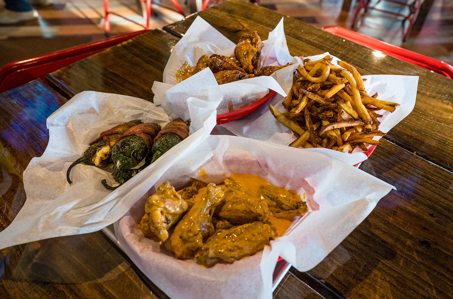 Baskets of sauced wings, fries, and bacon-wrapped jalapeño poppers on a table