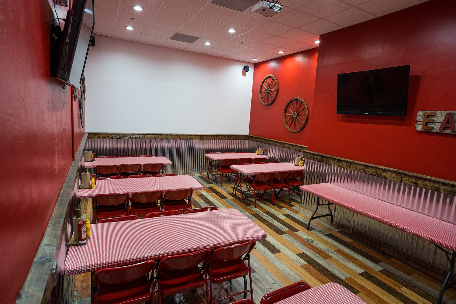 Wing Barn dining room with red chairs, wagon wheel decor, and wall-mounted TVs