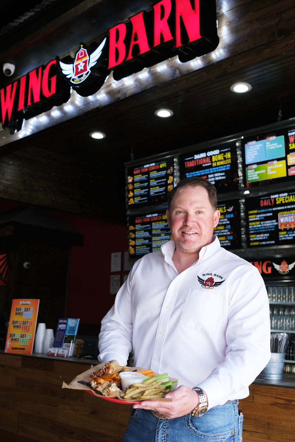 Wing Barn owner holding a basket of wings under the store's illuminated sign