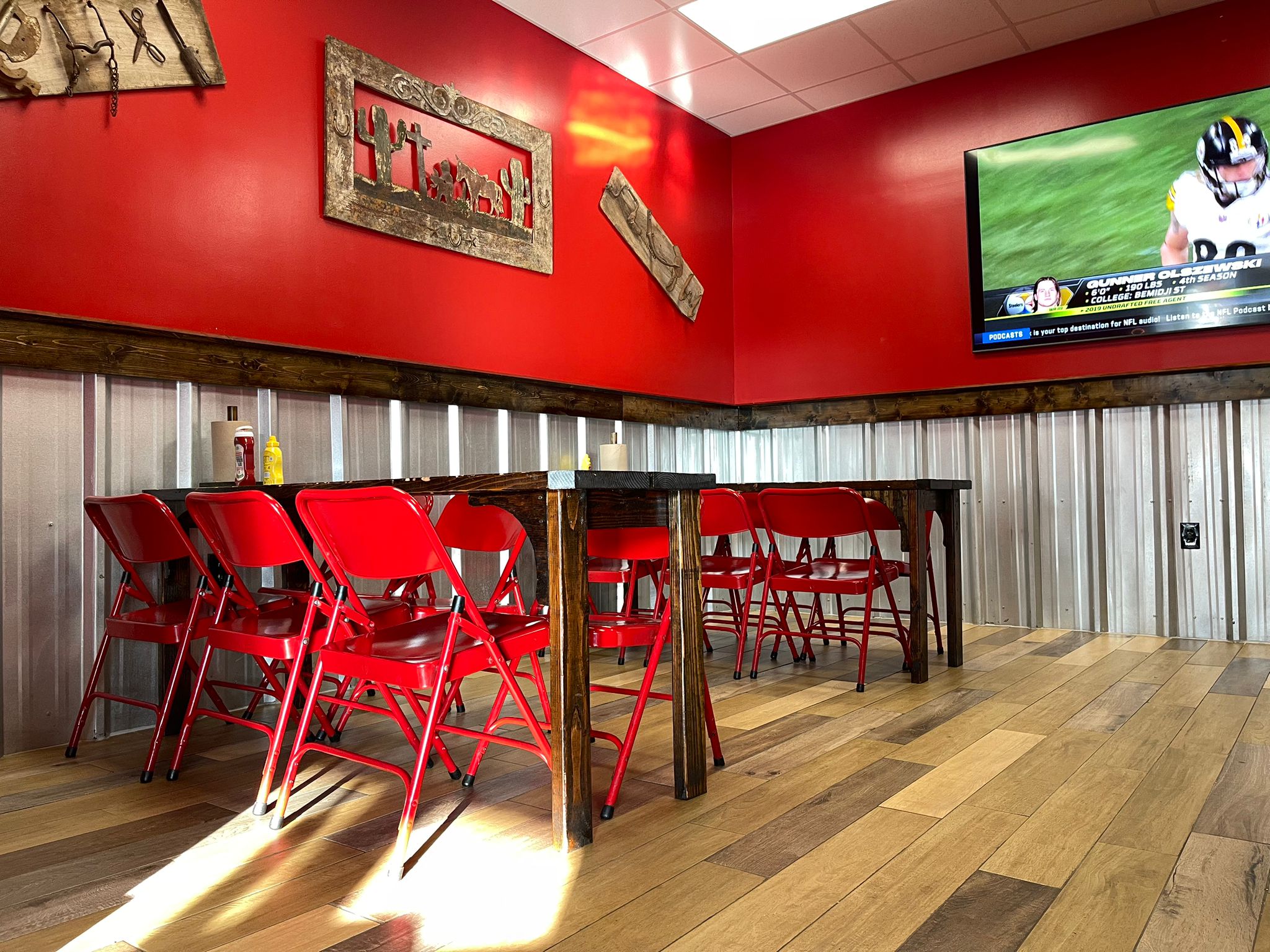 Wing Barn dining room with red walls, western wall art, and a TV showing football