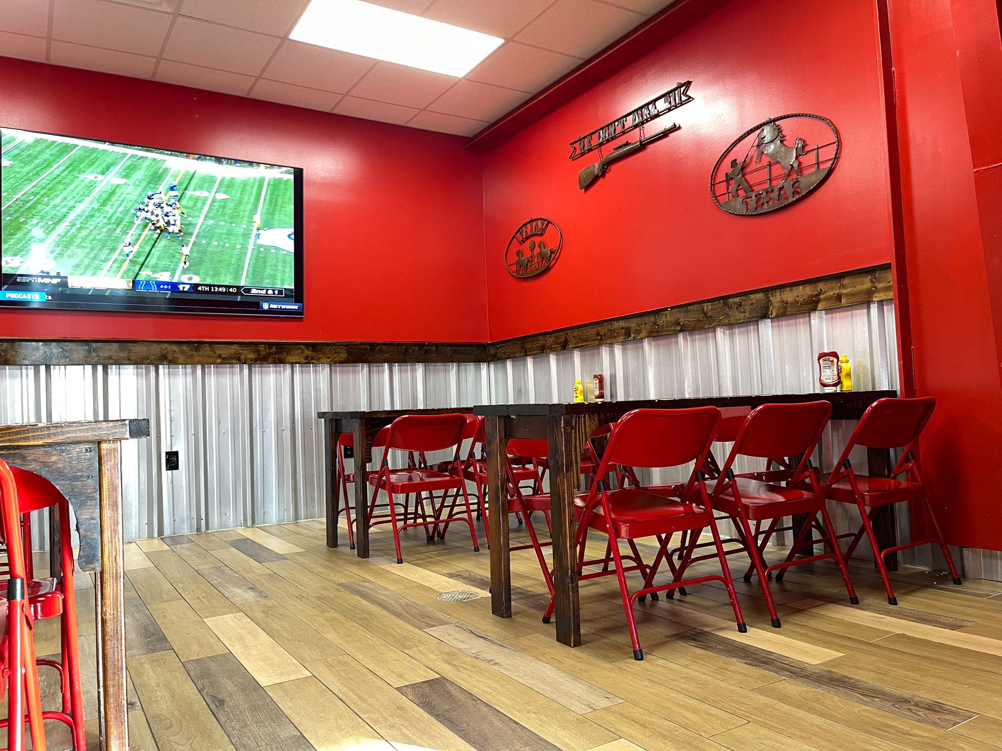 Wing Barn dining room with red walls, Texas wall art, and a TV showing football